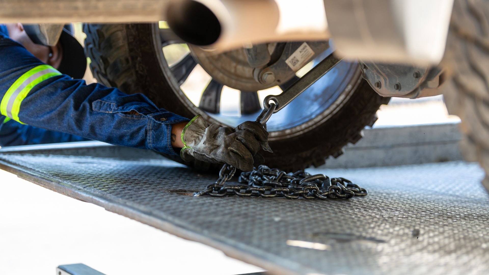 Worker secures chain near vehicle tire with safety gloves and reflective clothing