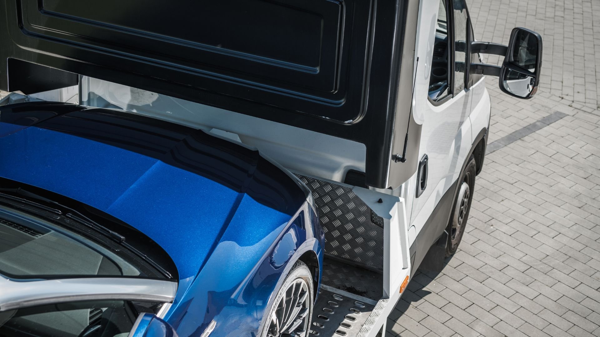 Blue sports car being loaded onto a white car transporter trailer