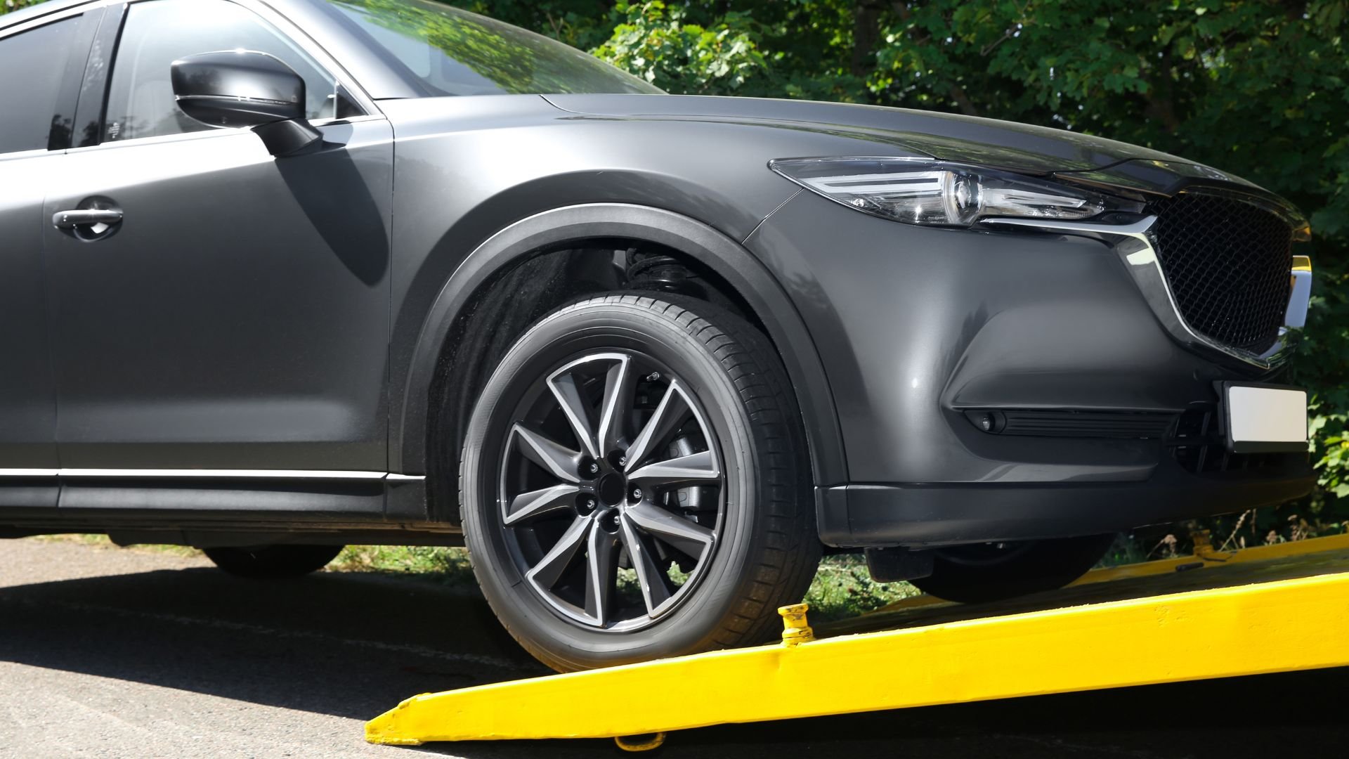 Gray SUV with stylish wheel parked on yellow platform near green trees