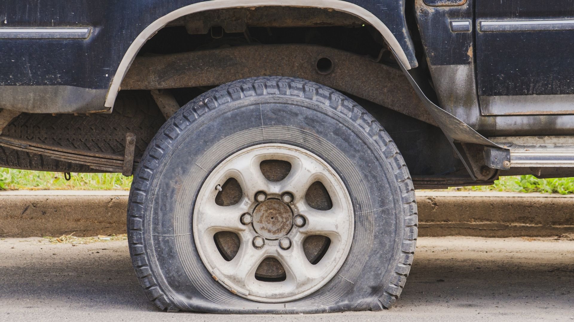 Flat tire on an old vehicle with a white wheel rim