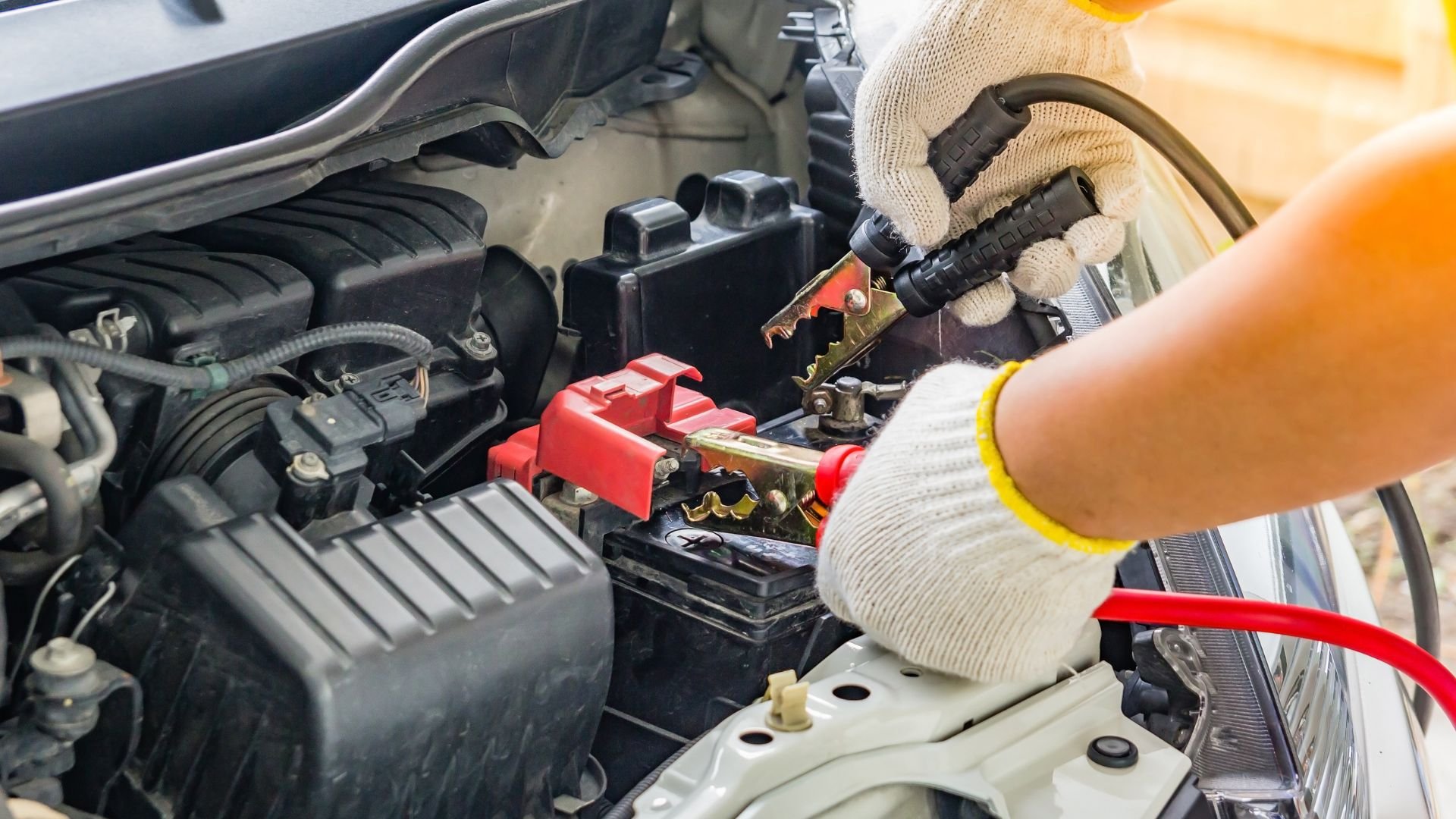 Mechanic connecting jumper cables to car battery in engine compartment