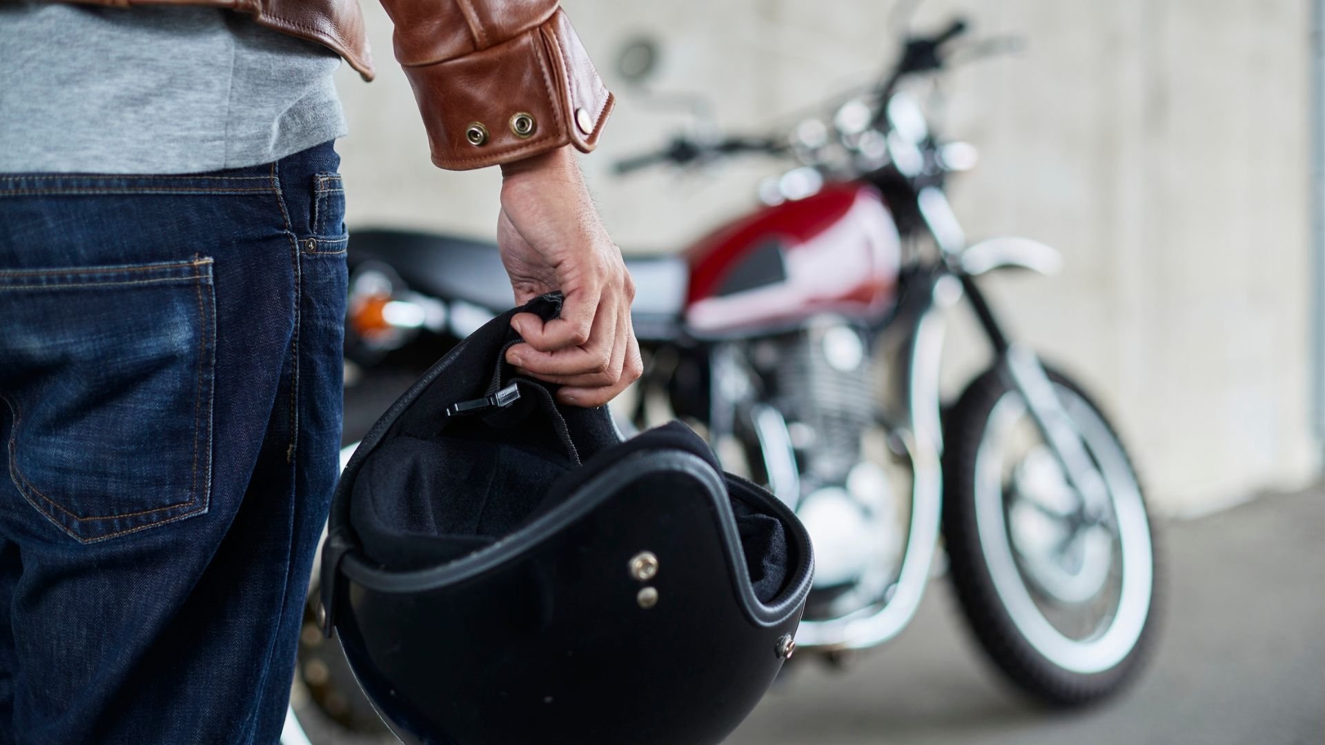 Motorcycle rider holding black helmet with classic bike in background