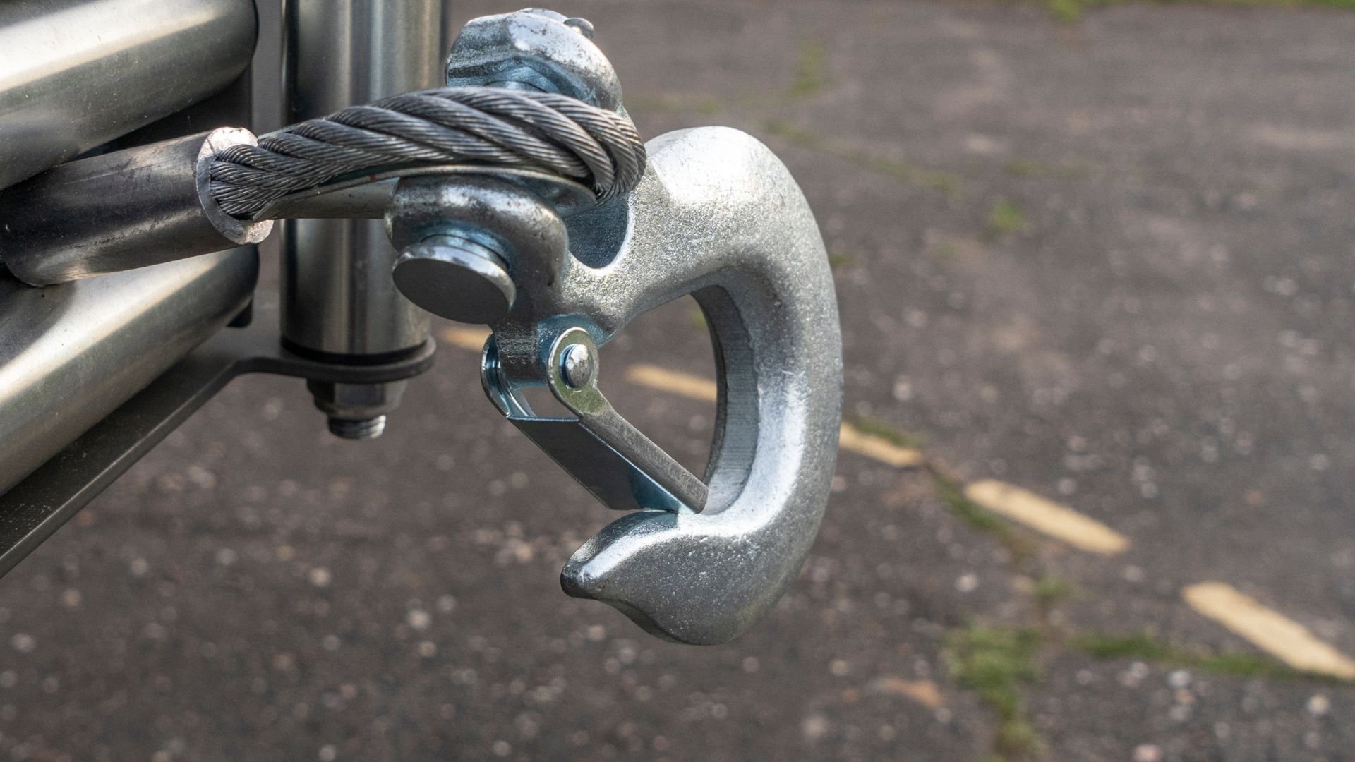 Steel cable hook attached to metal pole with blurred ground background
