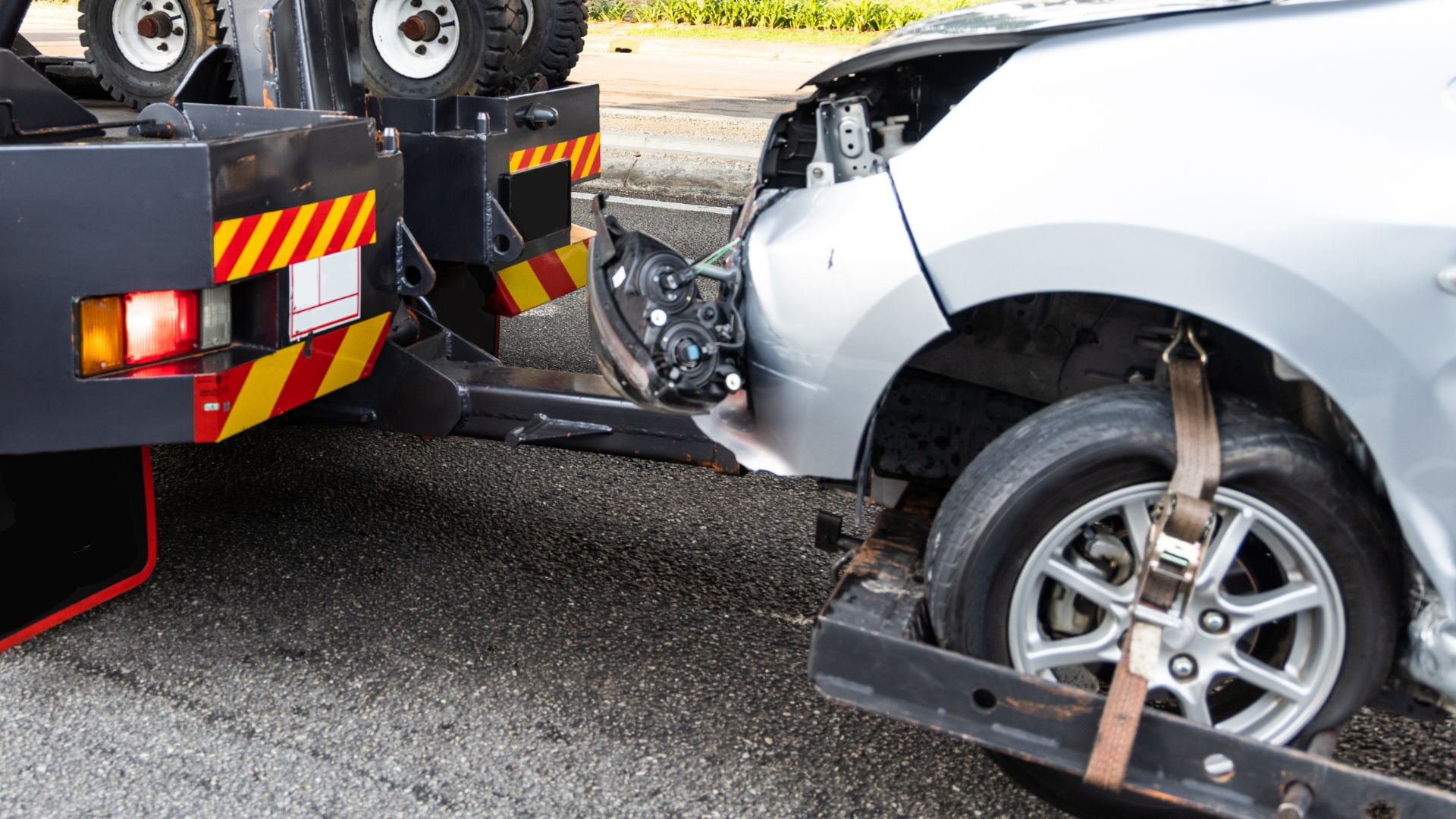Silver car being towed, secured by straps on a yellow and black truck